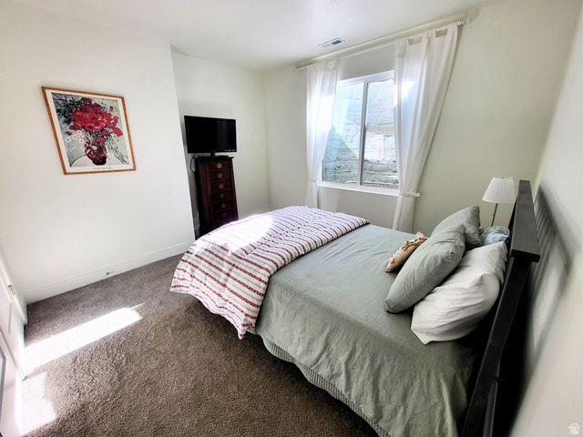 683 Kings Landing Tooele, UT 84074 - Photo 22 of 39 Carpeted room featuring a window with white drapes, white walls, and a black bed frame