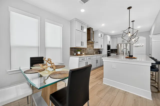 a kitchen with stainless steel appliances kitchen island granite countertop a sink dishwasher a stove a refrigerator and a dining table with wooden floor