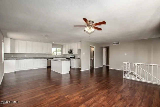 a view of an empty room with wooden floor and a kitchen