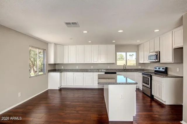 a kitchen with stainless steel appliances granite countertop a stove top oven a sink a refrigerator white cabinets and wooden floor