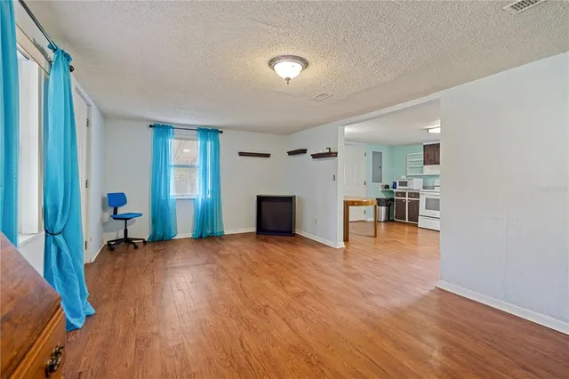 a view of empty room with wooden floor and kitchen