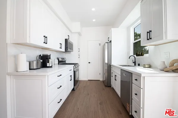 a kitchen with stainless steel appliances granite countertop a stove top oven a sink a dining table and chairs with wooden floor