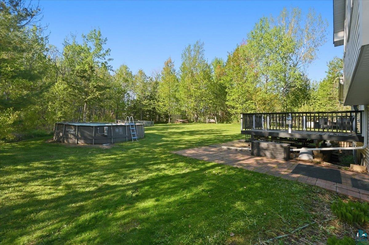 47 Amy Lane Esko, MN 55733 - Photo 25 of 33 Expansive backyard featuring a large above-ground pool, a spacious wood-finish deck with black railings, and a brick paver patio