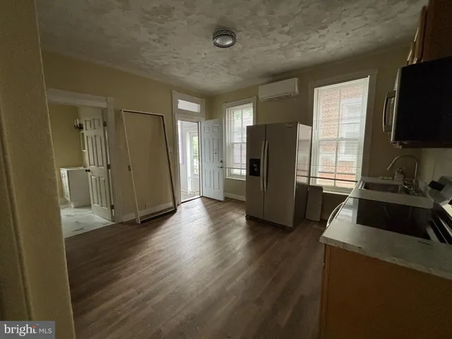 a view of a refrigerator in kitchen and an empty room with wooden floor windows