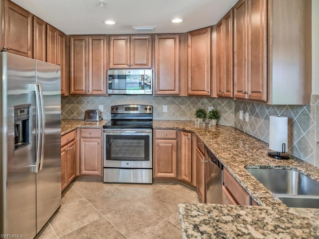 9114 Prima Way, Unit 102 Naples, FL 34113 - Photo 7 of 33 a kitchen with kitchen island granite countertop a stove sink and refrigerator