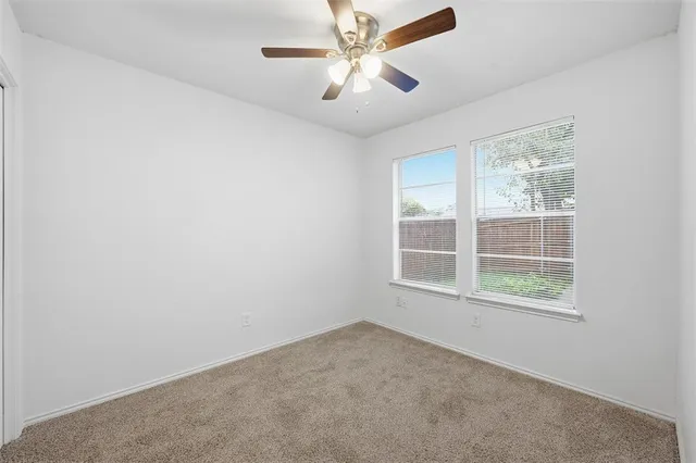 an empty room with chandelier fan and windows