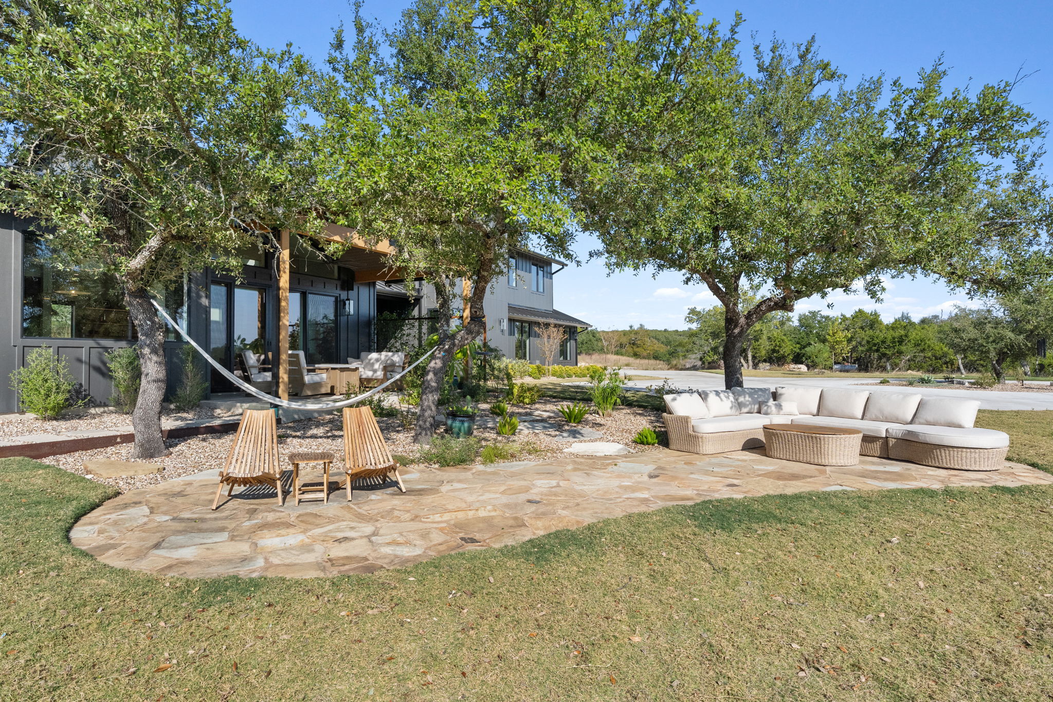 503 Happy Trail Dripping Springs, TX 78620 - Photo 32 of 38 Expansive flagstone patio with mature shade trees, a manicured lawn, and a modern exterior featuring large glass panels