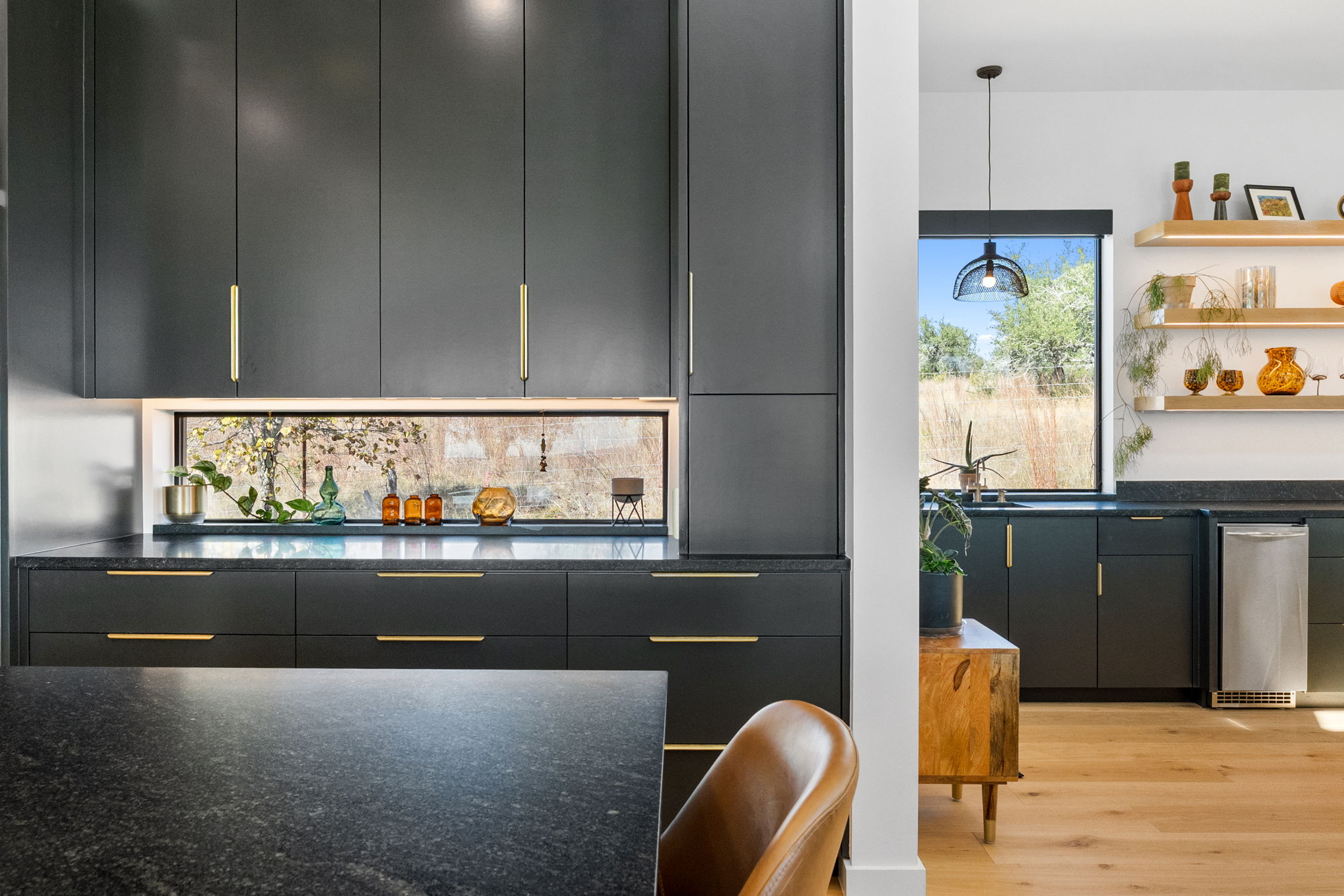 503 Happy Trail Dripping Springs, TX 78620 - Photo 10 of 38 Modern kitchen featuring dark cabinetry with gold-tone hardware, a horizontal window backsplash, and dark stone countertops
