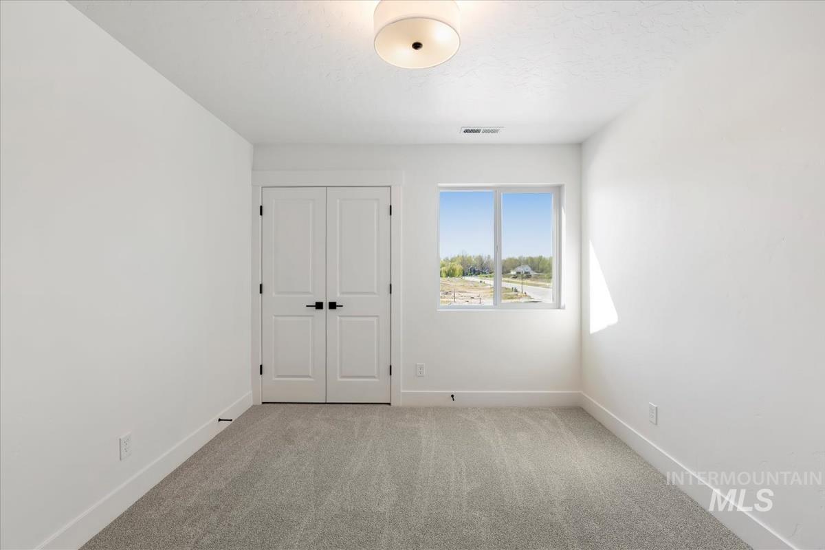 768 South Calhoun Lane Star, ID 83669 - Photo 27 of 36 Bright room featuring light grey carpet, a double-panel door with black hardware, a window with a natural landscape, a white ceiling with a flush-mount light fixture, and white walls with baseboards