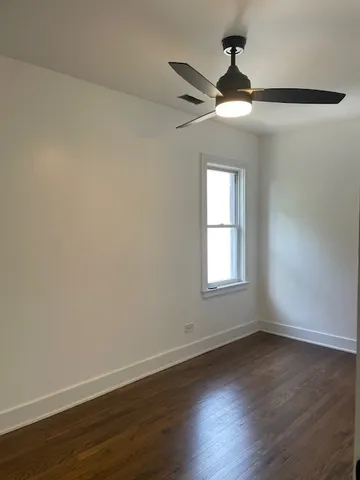 an empty room with wooden floor ceiling fan and windows