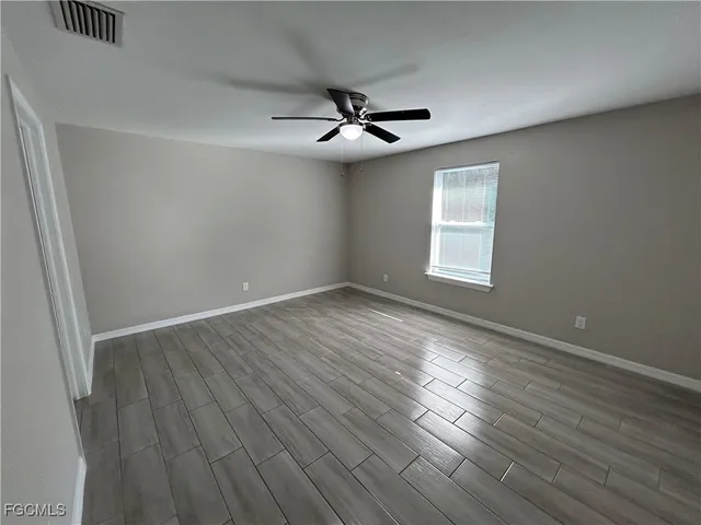 an empty room with wooden floor ceiling fan and windows