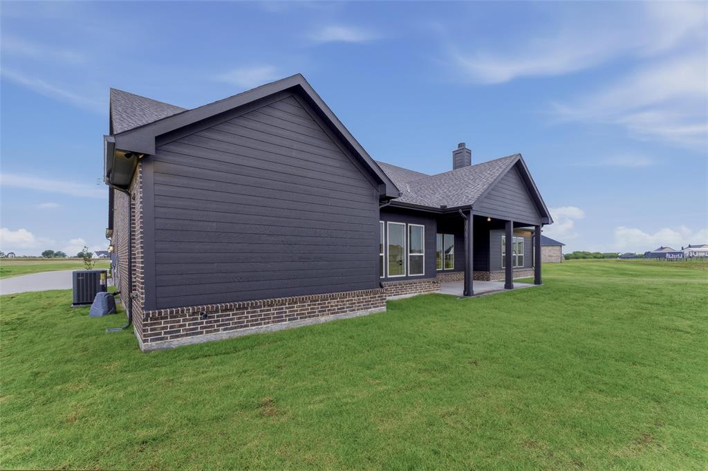 2208 Continent Court Krum, TX 76249 - Photo 25 of 26 Exterior featuring dark siding with brick wainscoting, an integrated covered patio with columns, a dark shingle roof, and multiple windows