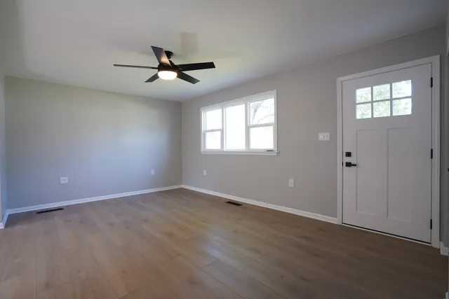 an empty room with wooden floor ceiling fan and windows