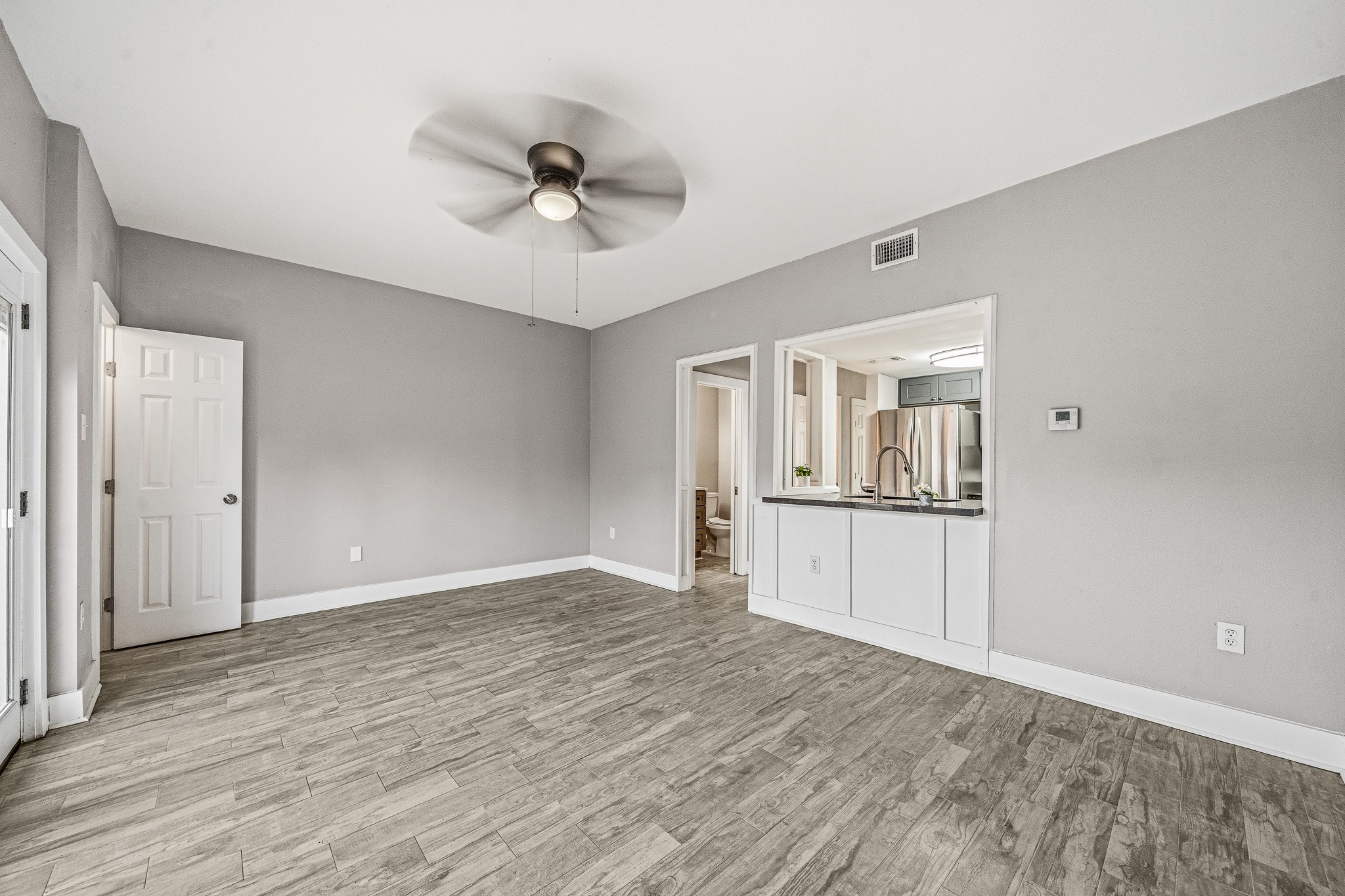 830 Threadneedle Street, Unit 240 Houston, TX 77079 - Photo 14 of 33 This room features modern wood-look flooring, a neutral color palette, and a ceiling fan. It opens to a kitchen with a pass-through window, and there is a visible door leading to another space, enhancing its functional layout.