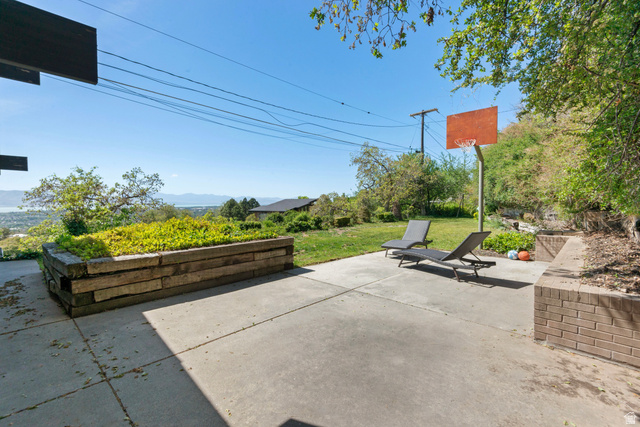 1900 North 100 East Provo, UT 84604 - Photo 40 of 49 Concrete patio area featuring a built-in planter box with lush greenery, brick retaining wall, and a full-size basketball hoop