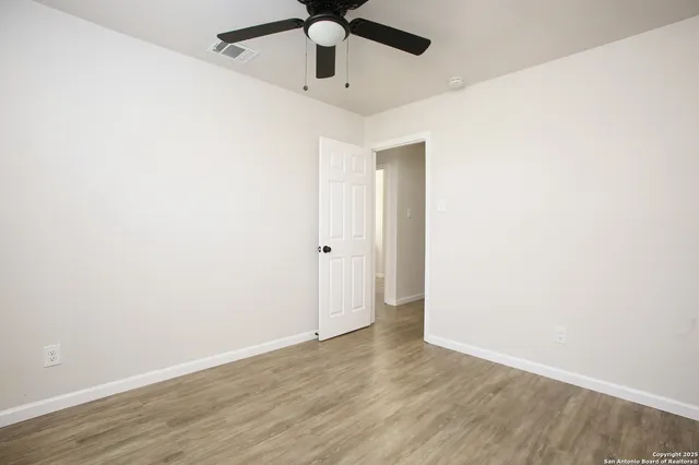 an empty room with wooden floor ceiling fan and window