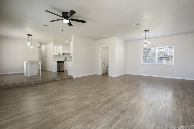 an empty room with wooden floor ceiling fan and windows