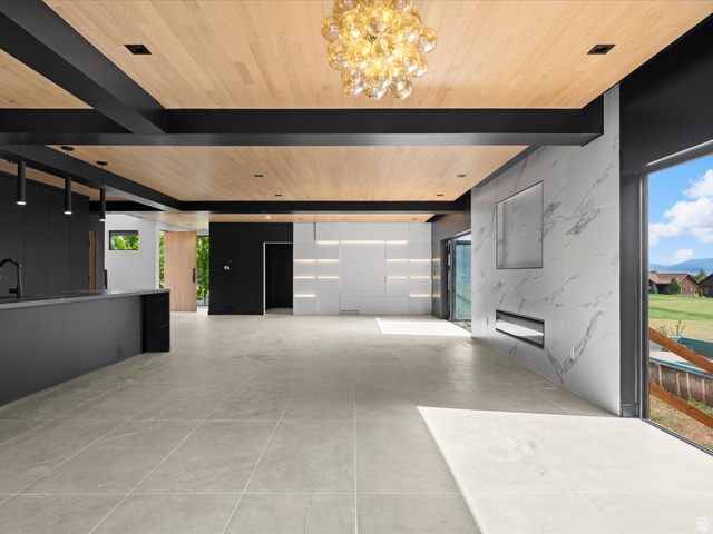 2610 Foxridge Road Garden City, UT 84028 - Photo 25 of 71 Wood-paneled ceiling with exposed black beams, large format floor tiling, built-in linear fireplace, integrated wall shelving with accent lighting, and a large sliding glass door