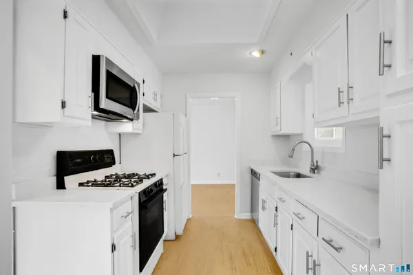 a kitchen with granite countertop a sink a stove top oven a refrigerator and cabinets