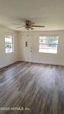 an empty room with wooden floor chandelier fan and windows