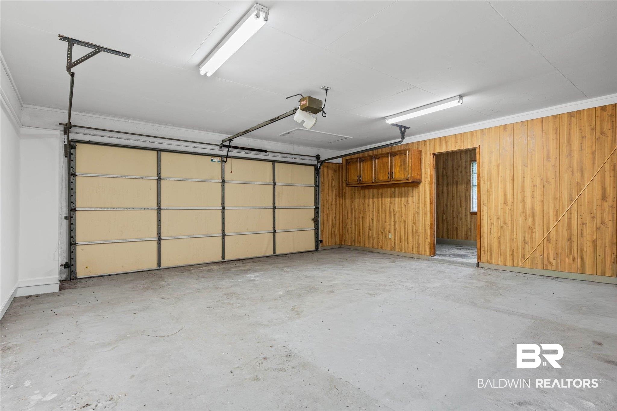 8301 Fordham Road Mobile, AL 36619 - Photo 27 of 57 Spacious garage featuring a sectional overhead door, concrete flooring, fluorescent ceiling lights, natural wood paneling, and an integrated storage cabinet