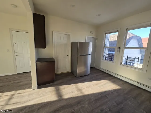 a view of a refrigerator in kitchen and an empty room with wooden floor windows