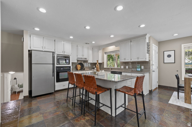 2370 Quail Run Circle East Sandy, UT 84093 - Photo 1 of 54 Kitchen featuring an island with stone countertop, white cabinetry, integrated stainless steel appliances, a tile backsplash, and multi-toned slate flooring