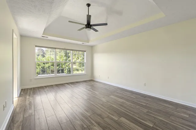 an empty room with wooden floor chandelier fan and windows