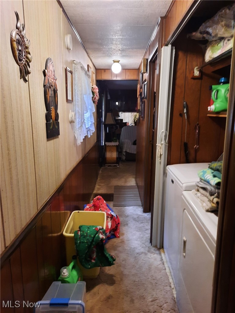 Corridor with light colored carpet, wooden walls, and washing machine and dryer