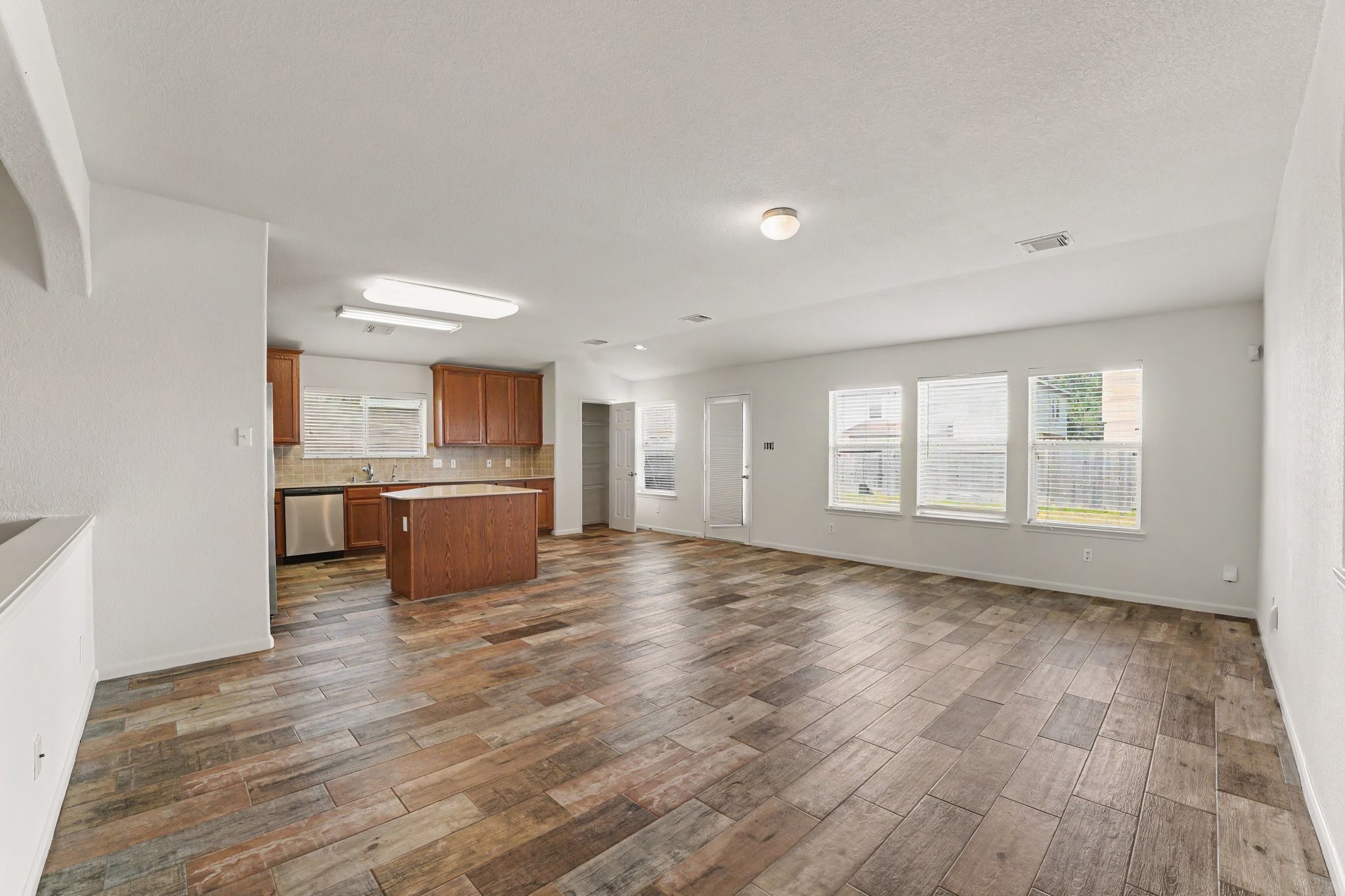 21427 Blooming Rock Lane Spring, TX 77379 - Photo 8 of 32 This spacious open-concept living area features a modern kitchen with stainless steel appliances and wooden cabinetry. The room is bright with large windows and has a stylish wood-look tile floor, providing a warm and inviting atmosphere.