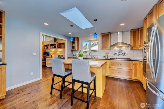 a kitchen with stainless steel appliances granite countertop a dining table chairs refrigerator and sink