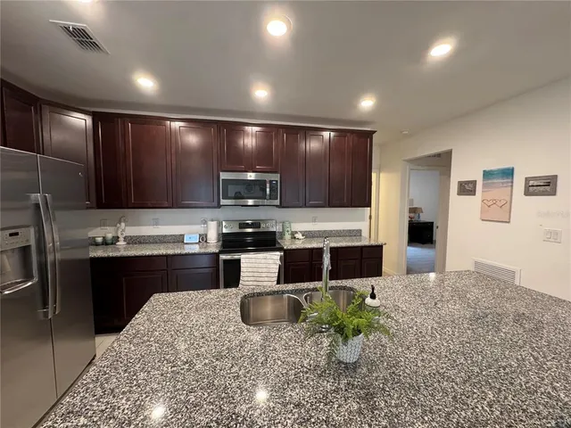 a large kitchen with stainless steel appliances kitchen island granite countertop a refrigerator oven a sink a stove a dining table and chairs