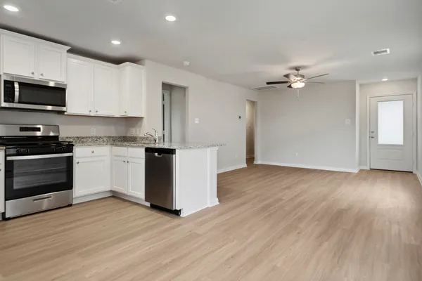 a kitchen with stainless steel appliances granite countertop a stove top oven a sink dishwasher and a refrigerator with wooden floor