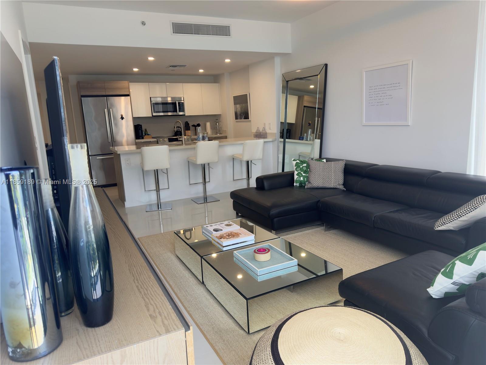 a living room with stainless steel appliances furniture a rug kitchen view and a kitchen island