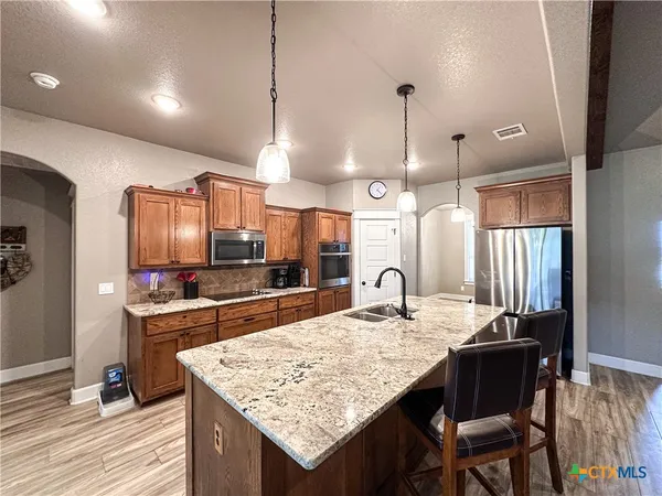 a kitchen with stainless steel appliances granite countertop a stove a sink dishwasher and a dining table with wooden floor