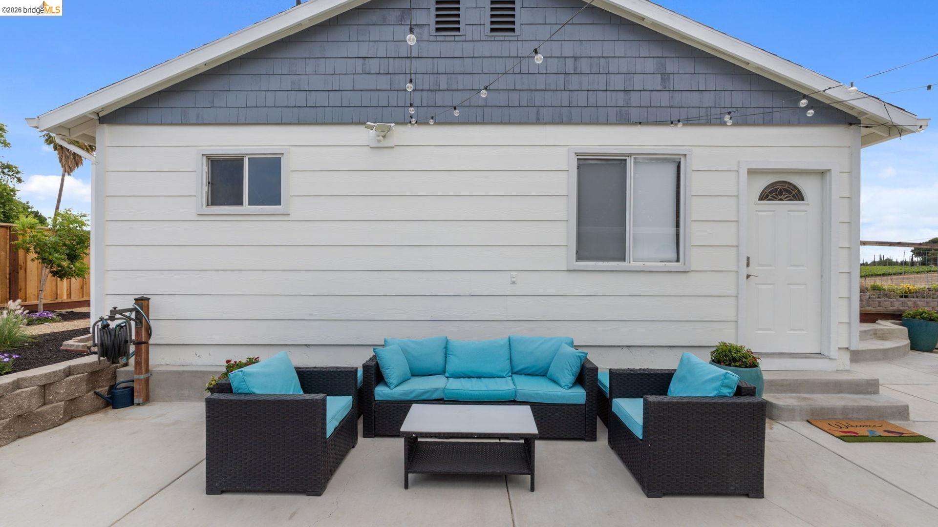 700 Brownstone Road Oakley, CA 94561 - Photo 36 of 58 Spacious concrete patio featuring a white siding exterior with a grey shingle gable, a built-in garden bed with stone retaining wall, and an arched panel door