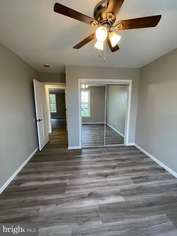 a view of an empty room with wooden floor and a ceiling fan