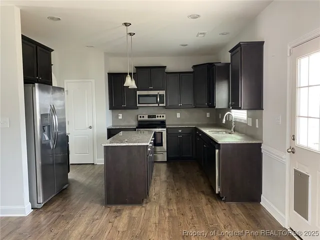 a kitchen with stainless steel appliances granite countertop a refrigerator a sink dishwasher a stove and a microwave oven on the wooden floor