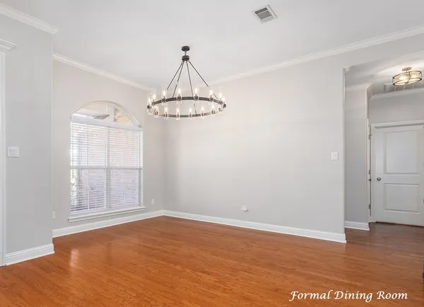 an empty room with wooden floor chandelier and windows
