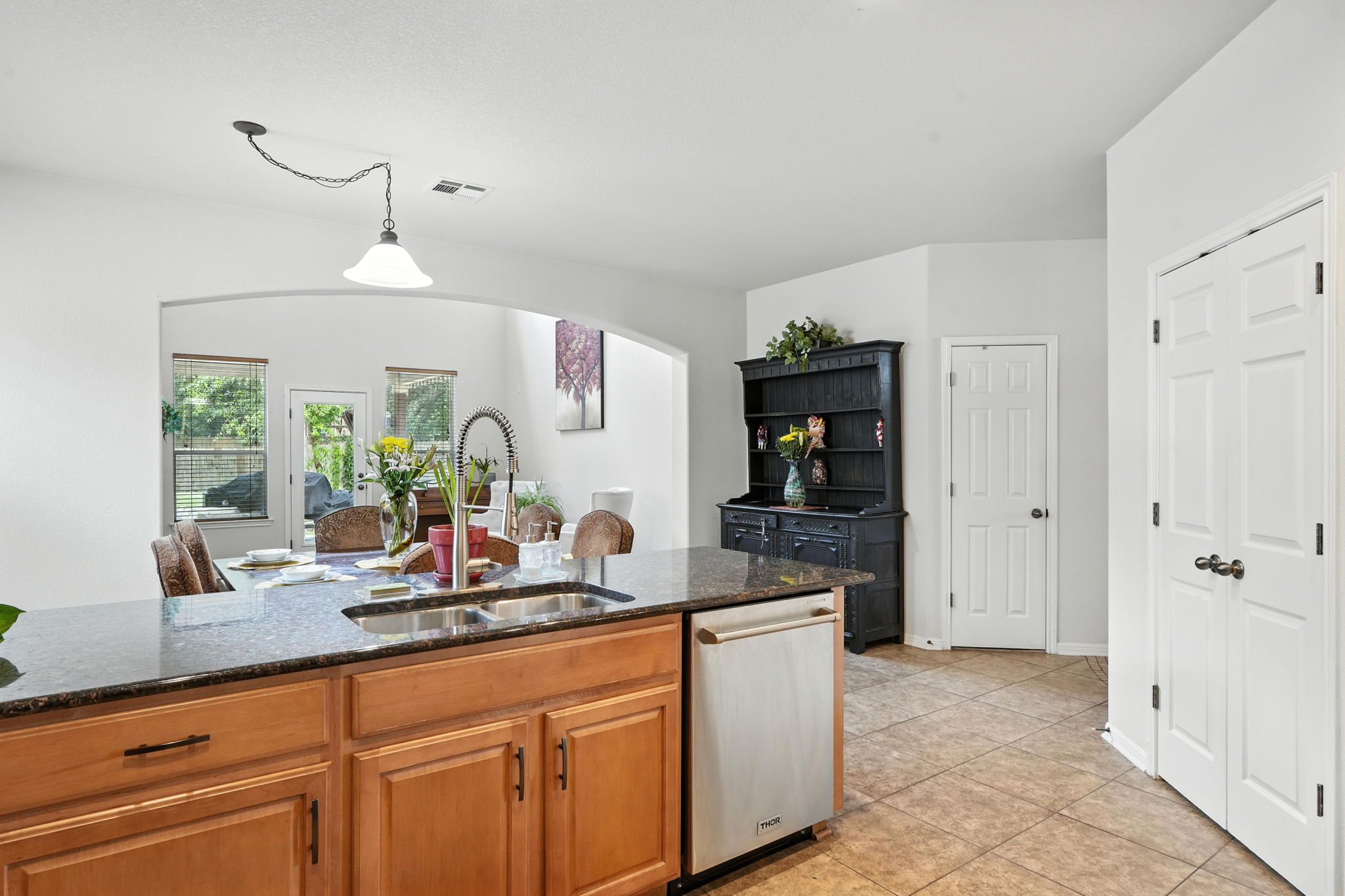 1802 Misty Ridge Leander, TX 78641 - Photo 13 of 39 Kitchen featuring dark stone counters, stainless steel dishwasher, decorative light fixtures, light tile patterned floors, and brown cabinetry