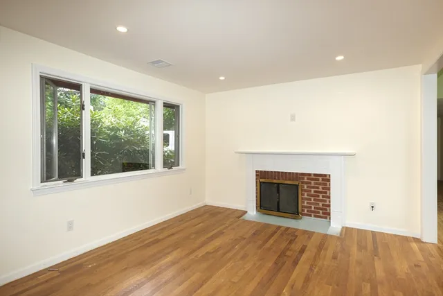 an empty room with wooden floor fireplace and windows
