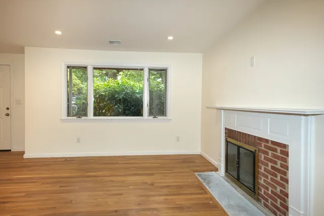 a view of an empty room with wooden floor fireplace and a window