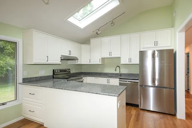 a kitchen with granite countertop a refrigerator a sink a stove and white cabinets