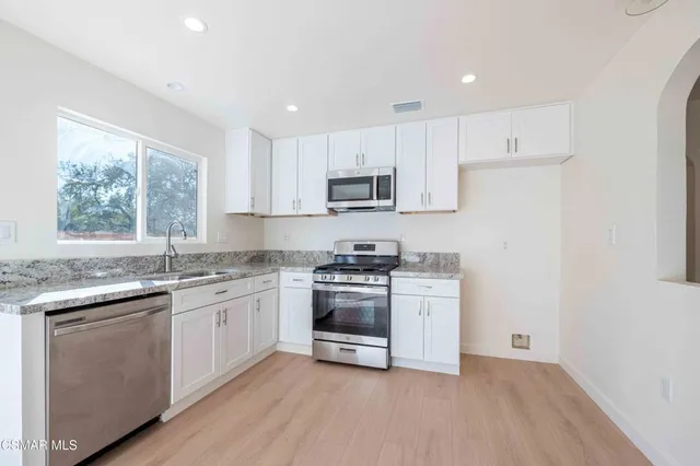 a kitchen with stainless steel appliances granite countertop a stove a sink and white cabinets