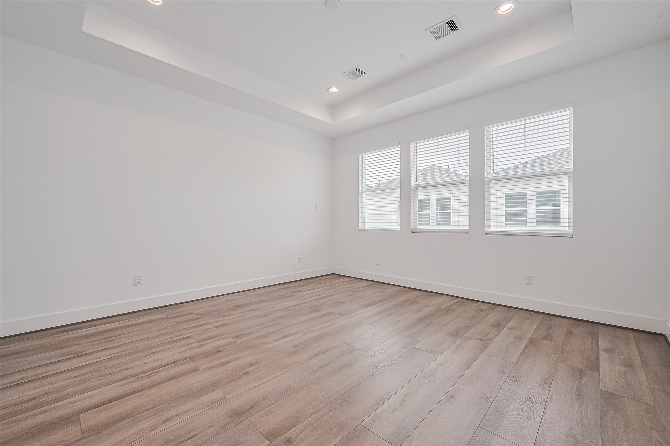 3510 Hadley Street Houston, TX 77004 - Photo 36 of 48 The primary bedroom is a tranquil retreat featuring a tray ceiling, wide windows, and warm lighting that enhances the natural wood floors. A serene and spacious layout sets the tone for rest and renewal.
