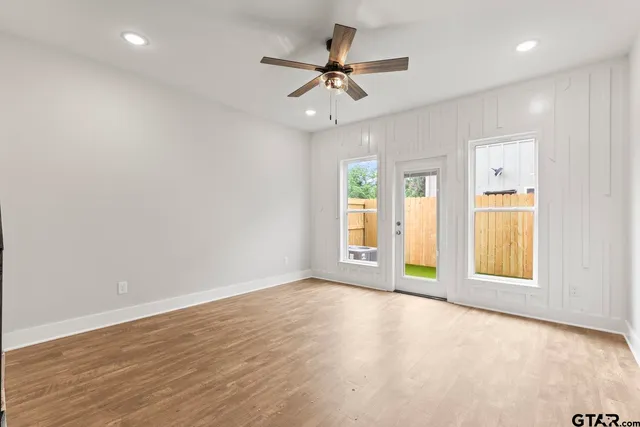 an empty room with wooden floor ceiling fan and windows