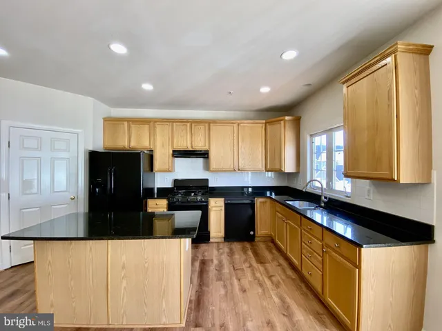 a kitchen with granite countertop a refrigerator a stove top oven a sink dishwasher and wooden cabinets