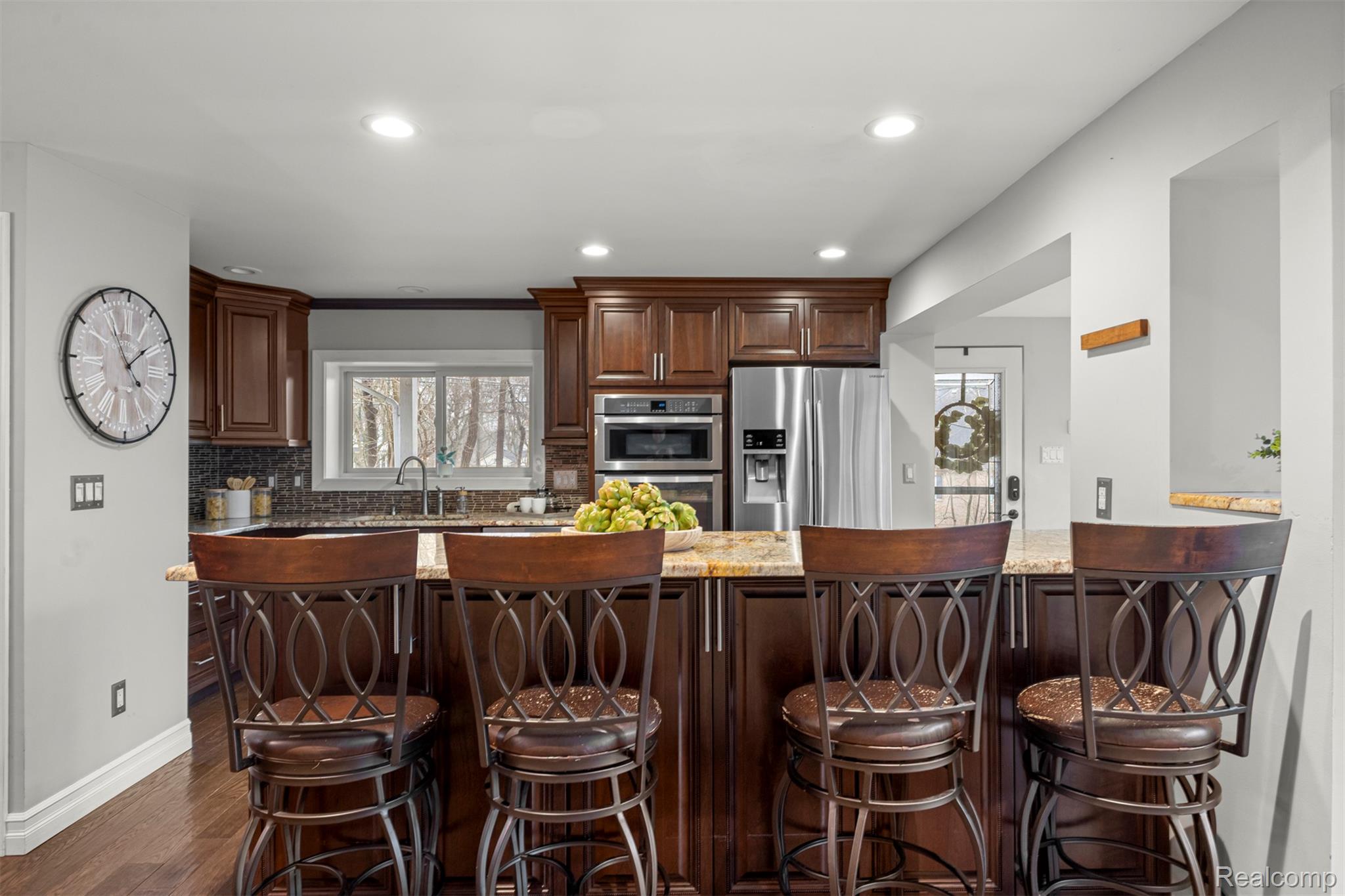 45401 West 9 Mile Road Novi, MI 48374 - Photo 11 of 67 Kitchen with dark brown cabinets, light stone countertops, appliances with stainless steel finishes, a kitchen bar, and decorative backsplash