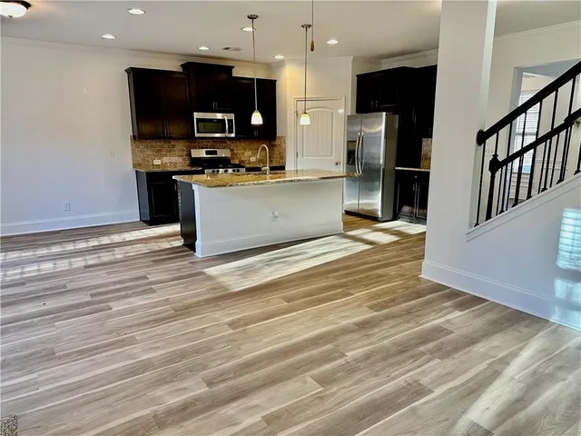 a large kitchen with stainless steel appliances kitchen island granite countertop a large stove a refrigerator a sink and dishwasher with wooden floor