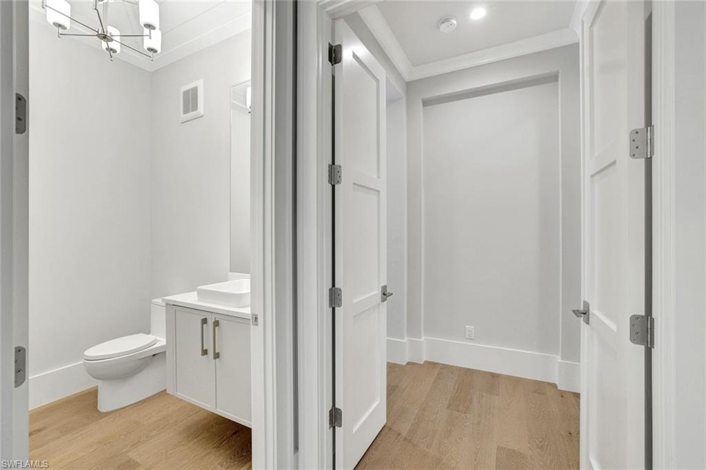 14286 Charthouse Circle Naples, FL 34114 - Photo 21 of 47 Half bathroom with vanity, light wood-style floors, crown molding, and a chandelier